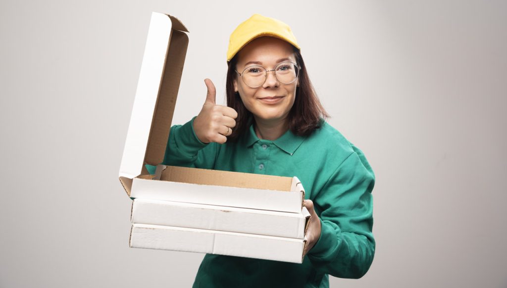 Una mujer sostiene 3 cajas de pizza. Empaques ecológicos la revolución silenciosa - Wisina